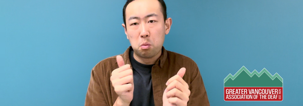 Paul ASL Video preview: A man with short dark hair stands against a teal blue background. He is wearing a dark t-shirt underneath an unbuttoned brown corduroy shirt. He has a neutral expression and looks toward the camera with his mouth slightly pursed. The framing is a medium shot capturing his head and shoulders in clear lighting.