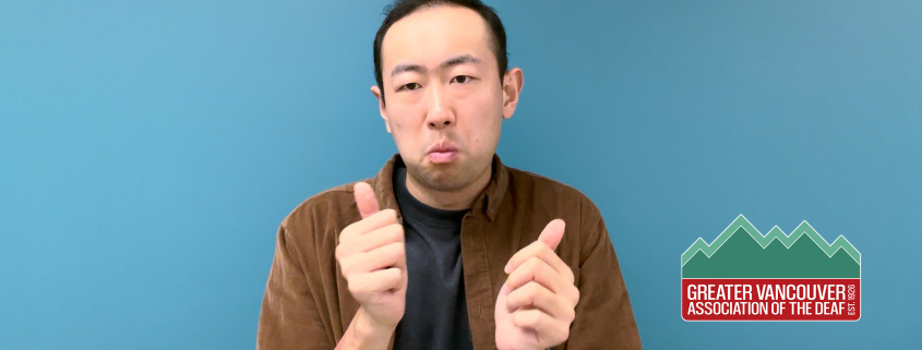 Paul ASL Video preview: A man with short dark hair stands against a teal blue background. He is wearing a dark t-shirt underneath an unbuttoned brown corduroy shirt. He has a neutral expression and looks toward the camera with his mouth slightly pursed. The framing is a medium shot capturing his head and shoulders in clear lighting.